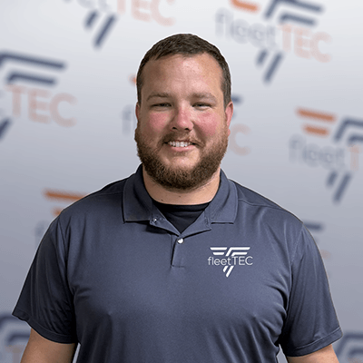 Smiling man in a fleetTEC polo shirt stands in front of a branded background.