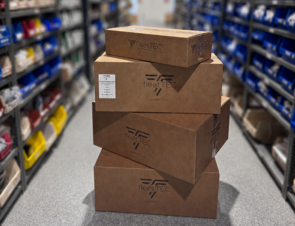 FleetTEC branded cardboard boxes stacked on the warehouse floor with organized inventory shelves in the background.